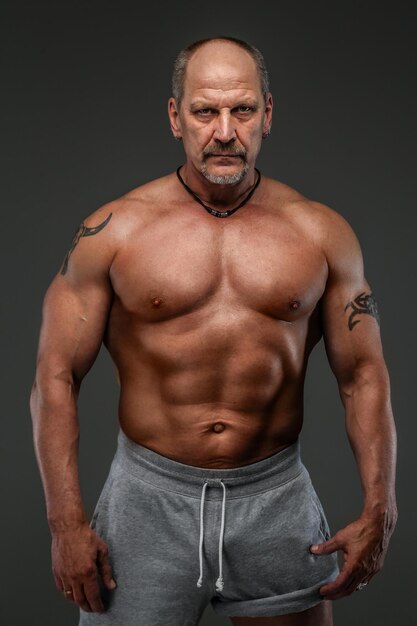 Strong muscular middle age man posing in studio. Isolated on grey.