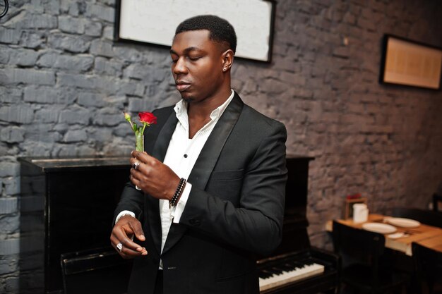 Strong powerful african american man in black suit sniff flower in test tube against piano