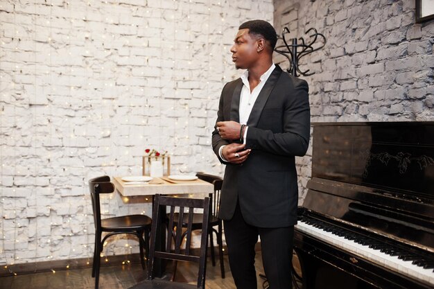 Strong powerful african american man in black suit standing against piano