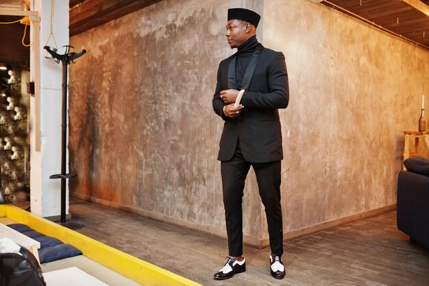 Strong powerful african american man in black suit and turtleneck and cap with elephant tusk