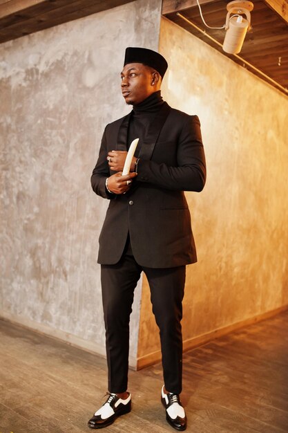 Strong powerful african american man in black suit and turtleneck and cap with elephant tusk