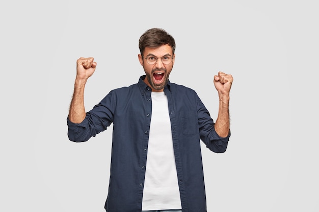 Strong powerful guy keeps hands raised clenched in fists, exclaims loudly from amazement, celebrates triumph