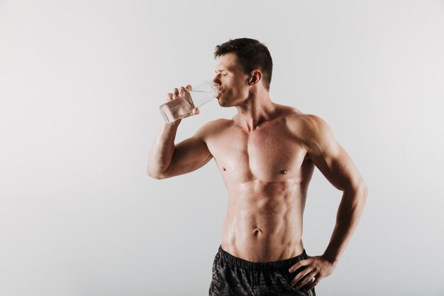 Strong serious young sportsman drinking water