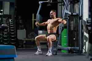 Free photo strong shirtless athlete sitting while training in crossover machine in gym side view of caucasian