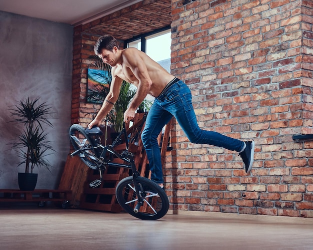 Strong shirtless man makes an acrobatic figure with BMX in a studio. Studio shot.