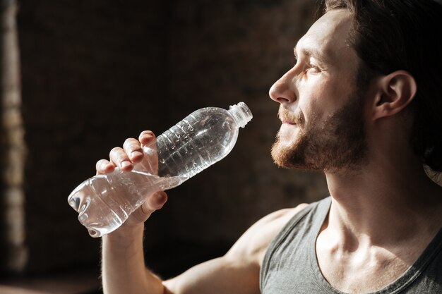 Strong sportsman in gym drinking water.