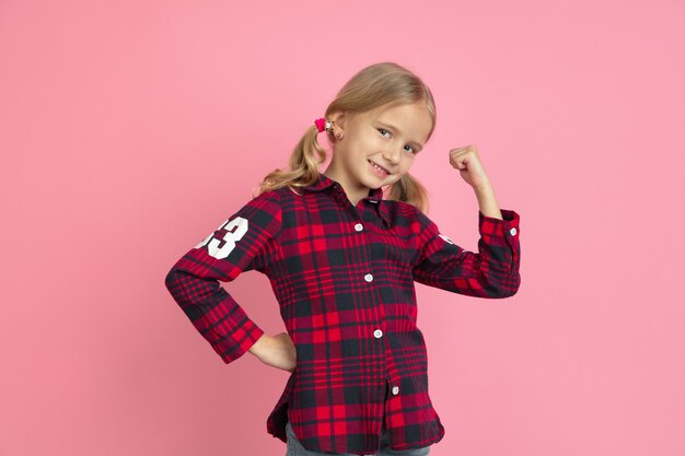 Strong, successful. Caucasian little girl's portrait on pink wall.