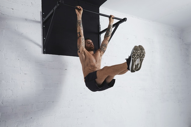 Strong tattooed athlete shows how to do calisthenic moves step by step Full leg rises on pull bar medium position