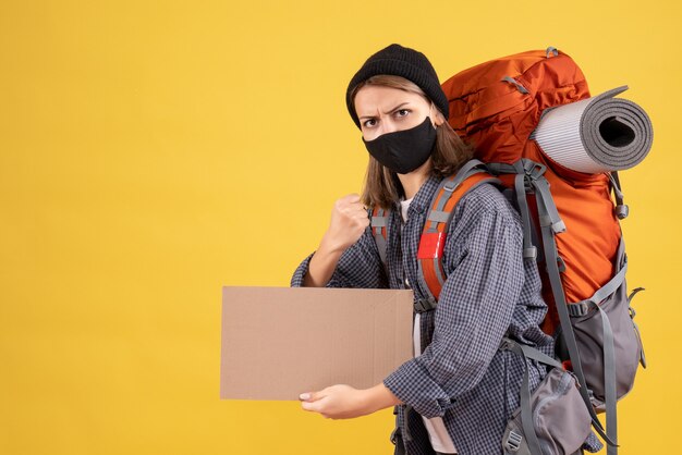 strong traveler woman with black mask and backpack holding cardboard