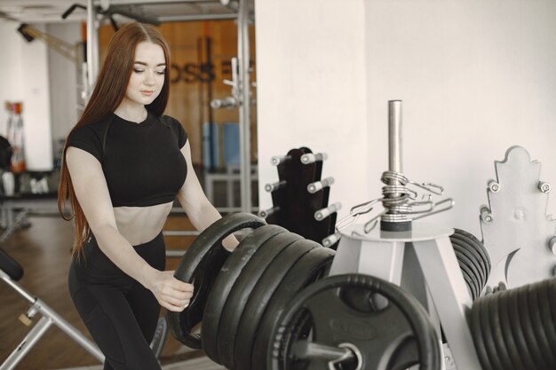 Strong woman's hands holding disc from barbell and putting it to the iron disks in gym. Muscular young woman holds iron disk of barbell.