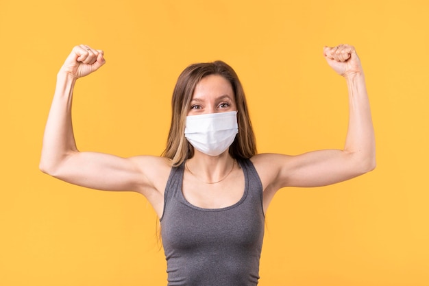 Сильная женщина с медицинской маской, показывающая ее мышцы