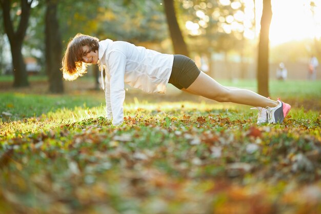 햇볕이 잘 드는 공원에서 판자 운동을 하는 강한 젊은 여성