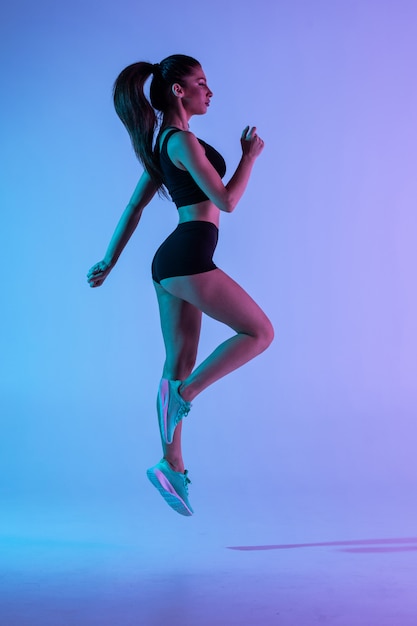 Сильный молодой спортивный женщина прыгать, изолированных на фиолетовые стены.