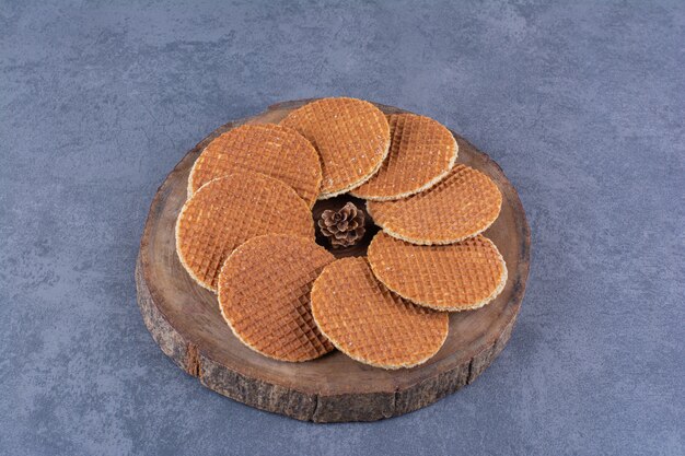 Stroopwafels with pinecone isolated in a wooden plate on a stone .High quality photo