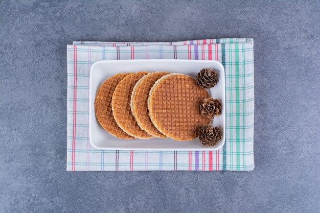 Бесплатное фото stroopwafels с шишками, изолированные в белой тарелке на камне.