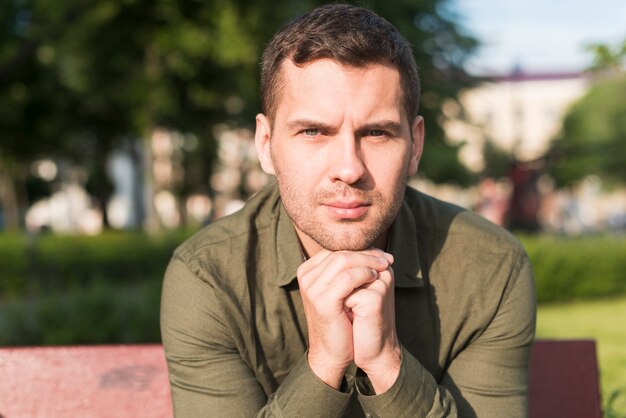 Stubble man sitting on bench looking at camera in park