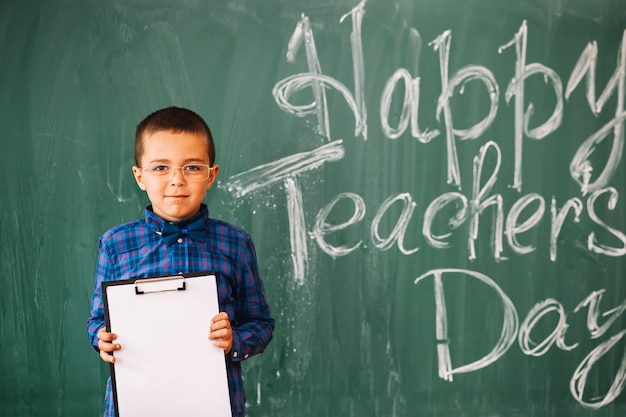 教師の日に黒板の背景に立っている学生の少年