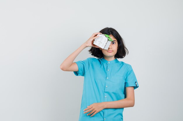 Student girl holding house model over her eyes in blue shirt