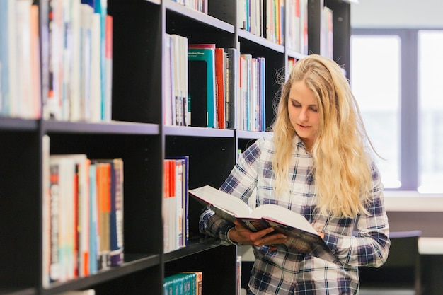 Student girl reading book by bookshelf