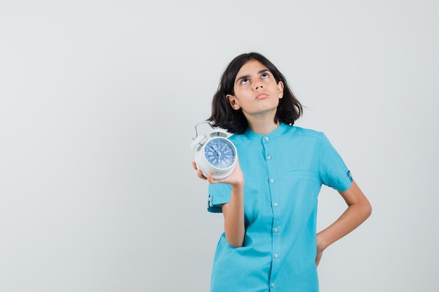 파란색 셔츠에 생각 하 고 집중 찾고있는 동안 시계를 보여주는 학생 소녀.