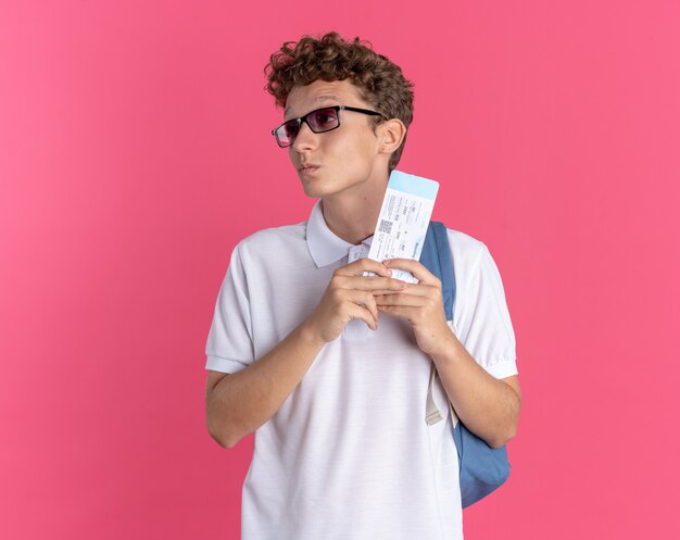 Student guy in casual clothing wearing glasses with backpack holding air ticket looking aside