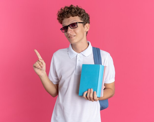 Student guy in casual clothing wearing glasses with backpack holding notebooks looking at camera