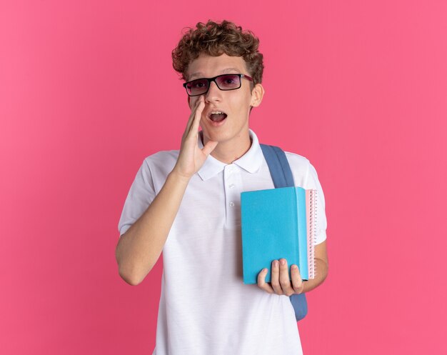 Student guy in casual clothing wearing glasses with backpack holding notebooks shouting