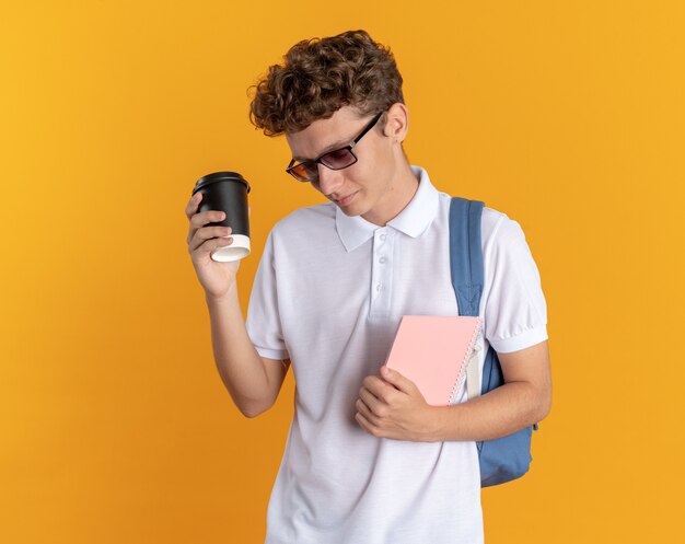 紙コップを保持しているバックパックと眼鏡をかけてカジュアルな服を着た学生の男
