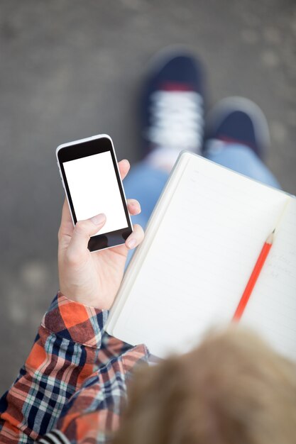 Student holding a smartphone against an open copybook