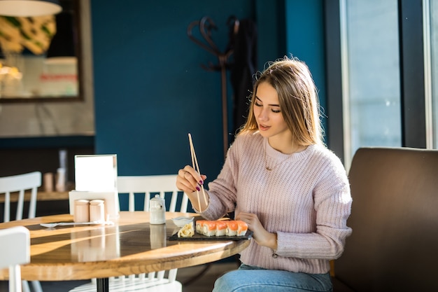 Student lady in white sweater eating sushi for lunch at a small caffe