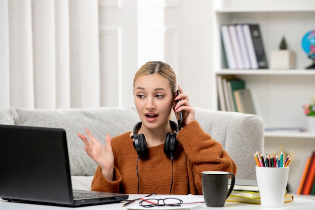 Studente online ragazza carina con gli occhiali e maglione che studia sul computer durante la telefonata