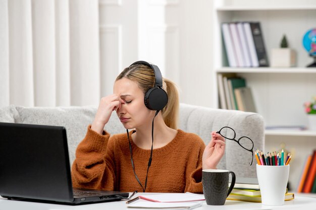 眼鏡とセーターを脱いでコンピュータで勉強している学生のオンラインかわいい女の子