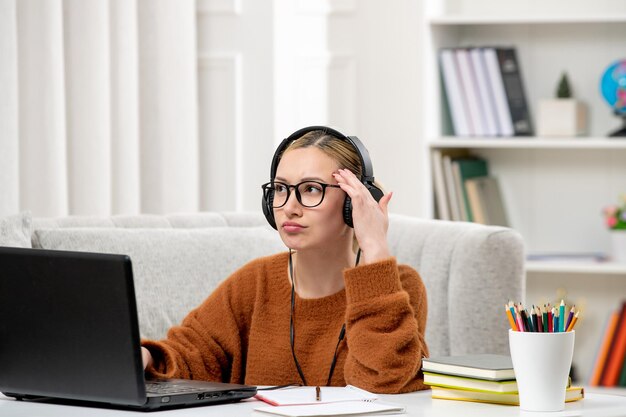 헤드폰으로 생각하는 컴퓨터에서 공부하는 안경과 스웨터를 입은 온라인 귀여운 소녀