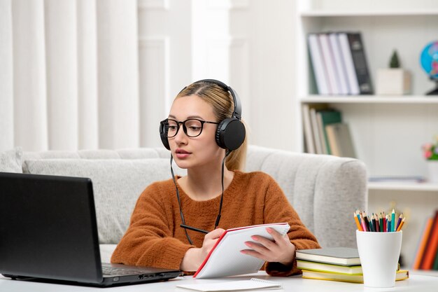 ノートを書くコンピュータで勉強している眼鏡とセーターの学生オンラインかわいい女の子