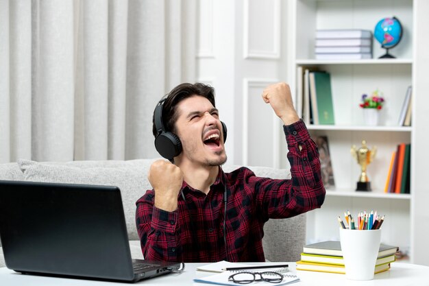 幸せで興奮しているコンピュータで勉強している眼鏡をかけたチェックシャツの学生オンラインかわいい男