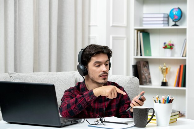 Student online cute guy in checked shirt with glasses studying on computer looking at the phone