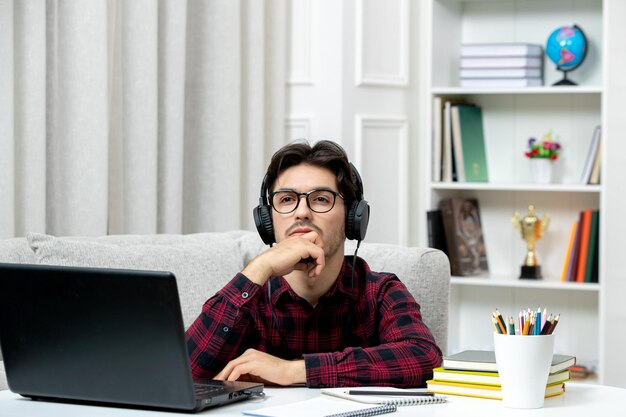Студент онлайн симпатичный парень в клетчатой рубашке в очках учится на компьютере, глядя вверх