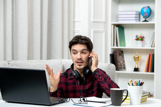 電話でコンピューターで勉強している眼鏡をかけたチェックシャツの学生オンラインかわいい男