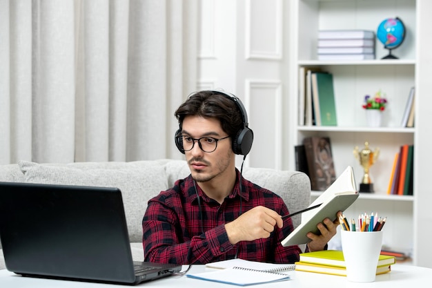책을 읽고 컴퓨터에서 공부하는 안경을 쓴 체크 셔츠를 입은 온라인 귀여운 남자