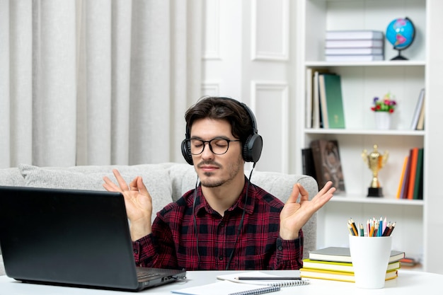 禅のジェスチャーを示すコンピューターで勉強している眼鏡をかけたチェックシャツの学生オンラインかわいい男