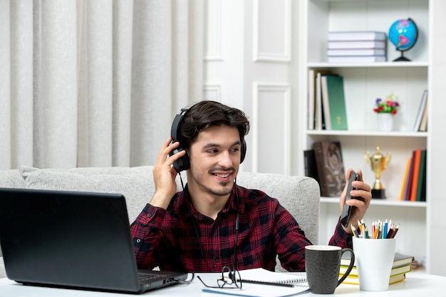 Student online cute guy in checked shirt with glasses studying on computer smiling and on phone