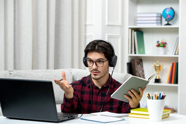 Студент онлайн симпатичный парень в клетчатой рубашке в очках учится на компьютере, машет руками