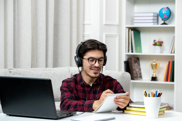 ノートを書くコンピュータで勉強している眼鏡をかけたチェックシャツの学生オンラインかわいい男