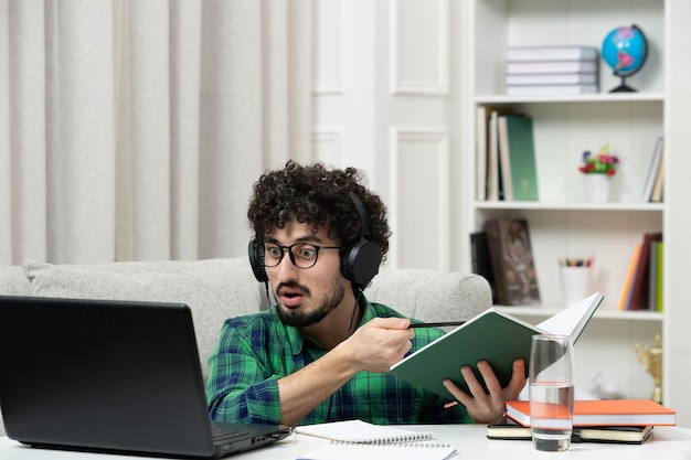 Студент онлайн милый молодой парень учится на компьютере в очках в зеленой рубашке с блокнотом