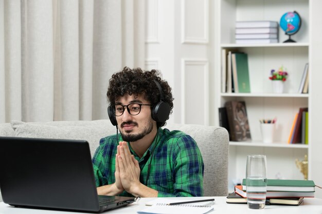 Student online cute young guy studying on computer in glasses in green shirt praying