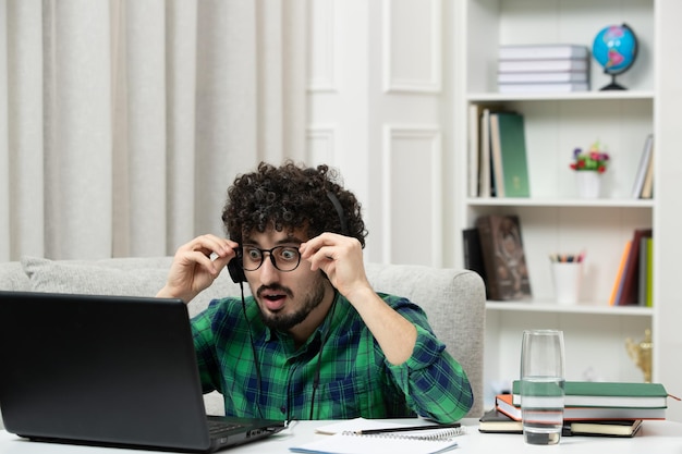 Foto gratuita studente online carino giovane ragazzo che studia al computer con gli occhiali in camicia verde scioccato