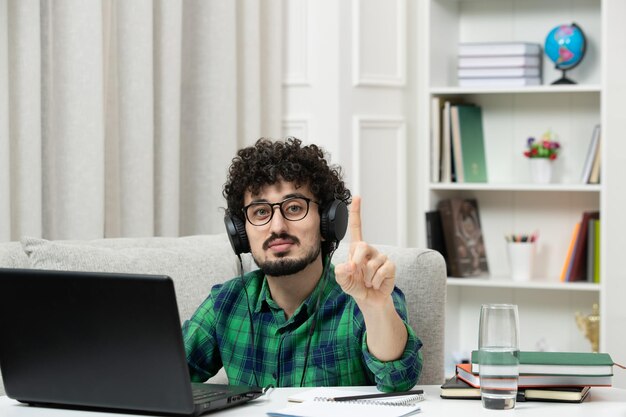 1分を示す緑のシャツのメガネでコンピューターで勉強している学生オンラインかわいい若い男