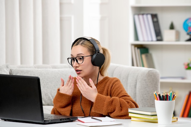 Студент онлайн молодая милая девушка в очках и оранжевом свитере учится на компьютере в шоке
