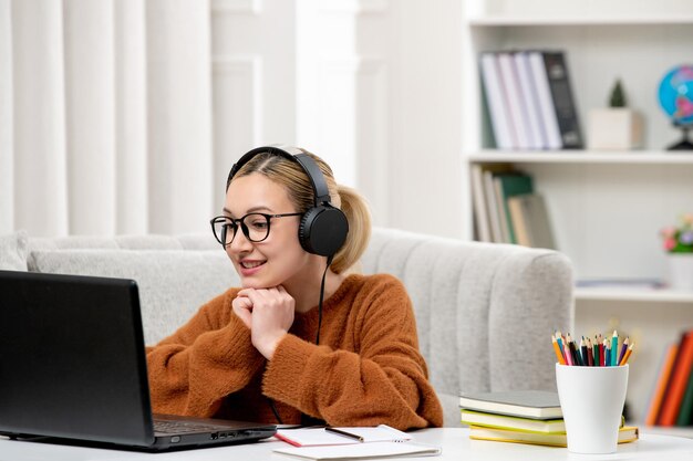 Student online young cute girl in glasses and orange sweater studying on computer smiling happily