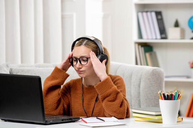 疲れたコンピュータで勉強している眼鏡とオレンジ色のセーターの学生オンライン若いかわいい女の子